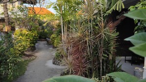 Un étroit sentier bordé d’une végétation luxuriante et un bâtiment doté d’un toit en tuiles.