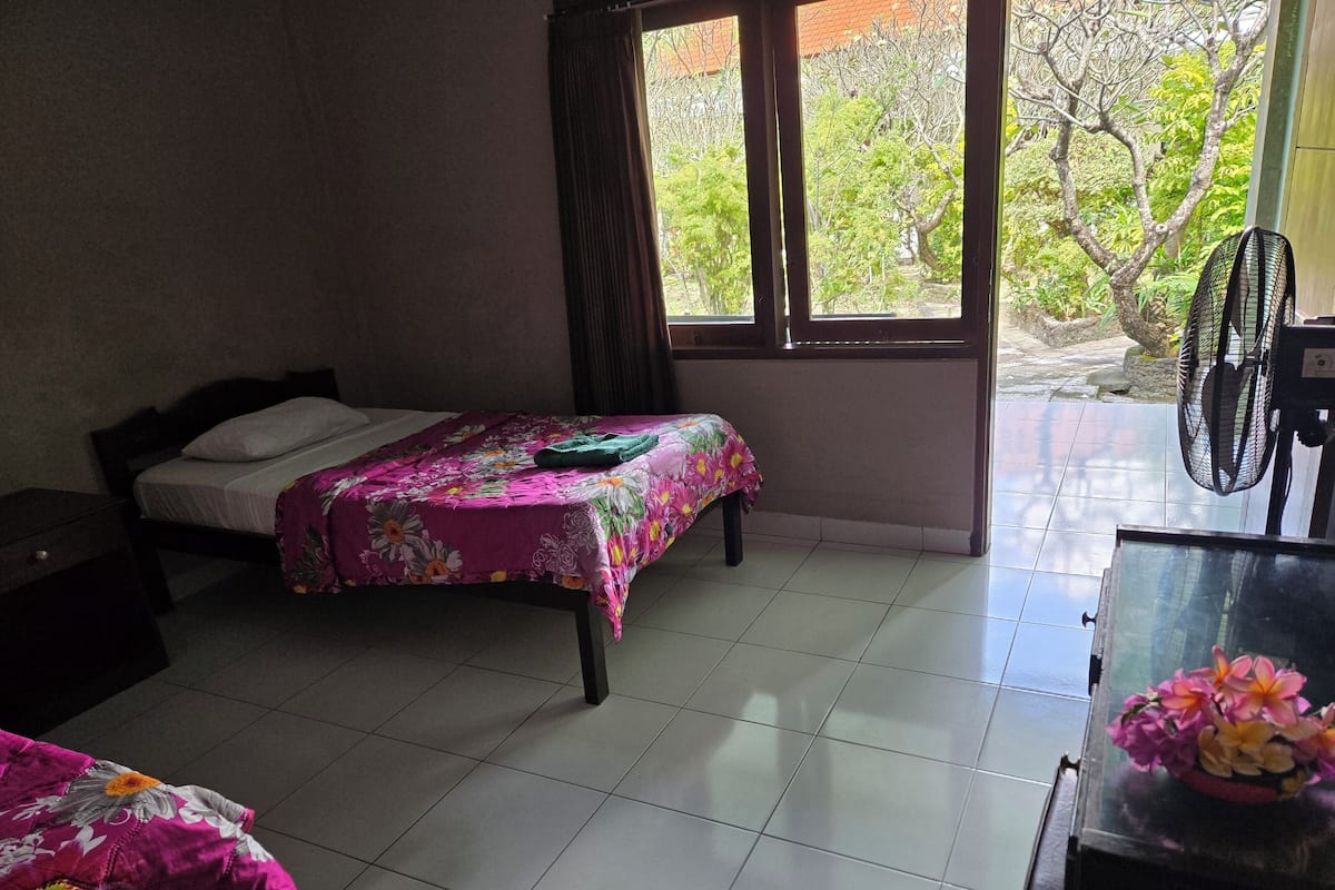 A bedroom with two beds, a desk, and a window with a view of greenery.