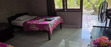 A bedroom with two beds, a desk, and a window with a view of greenery.