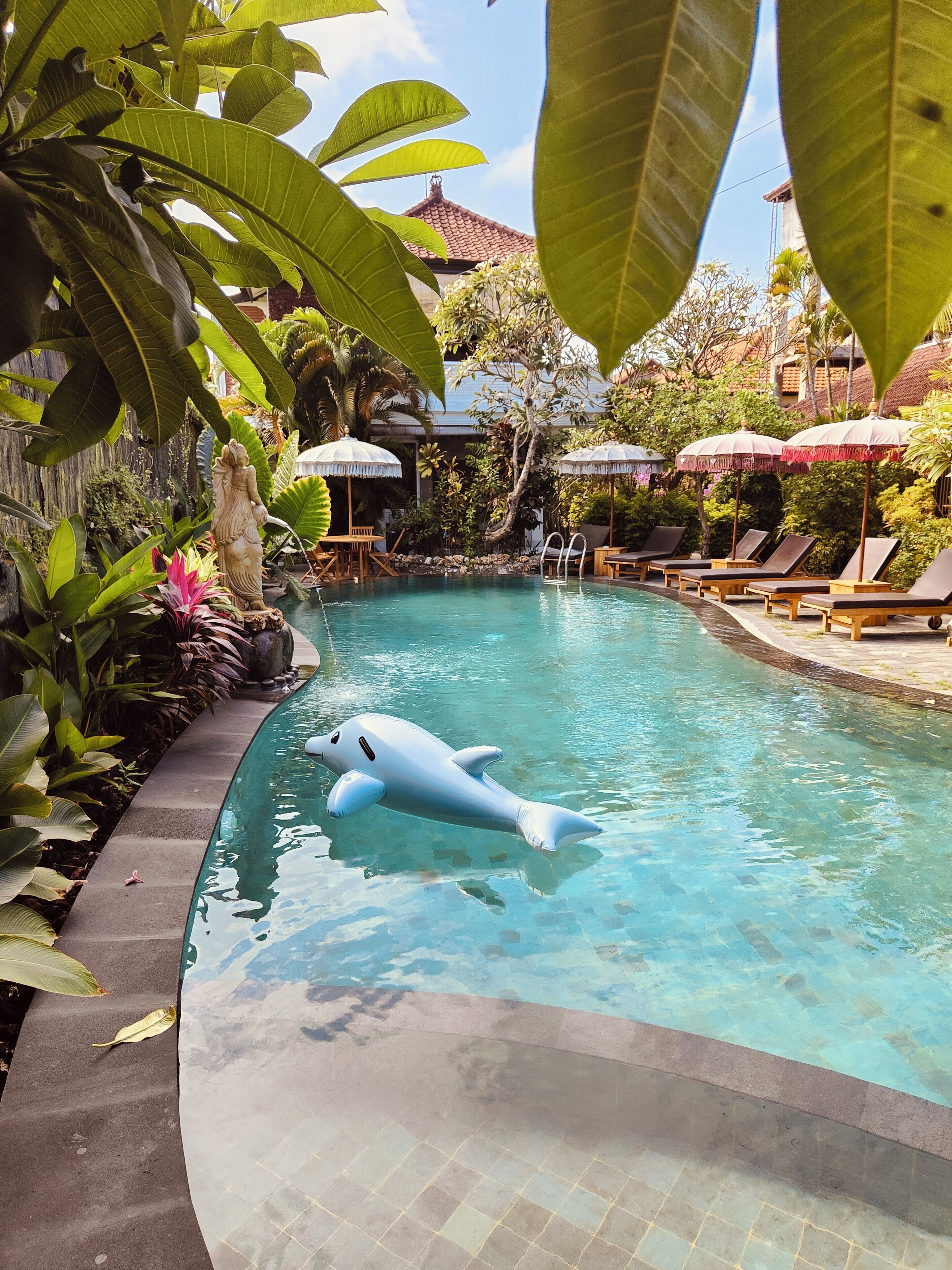 A swimming pool with a dolphin float, surrounded by lush greenery and outdoor seating areas.