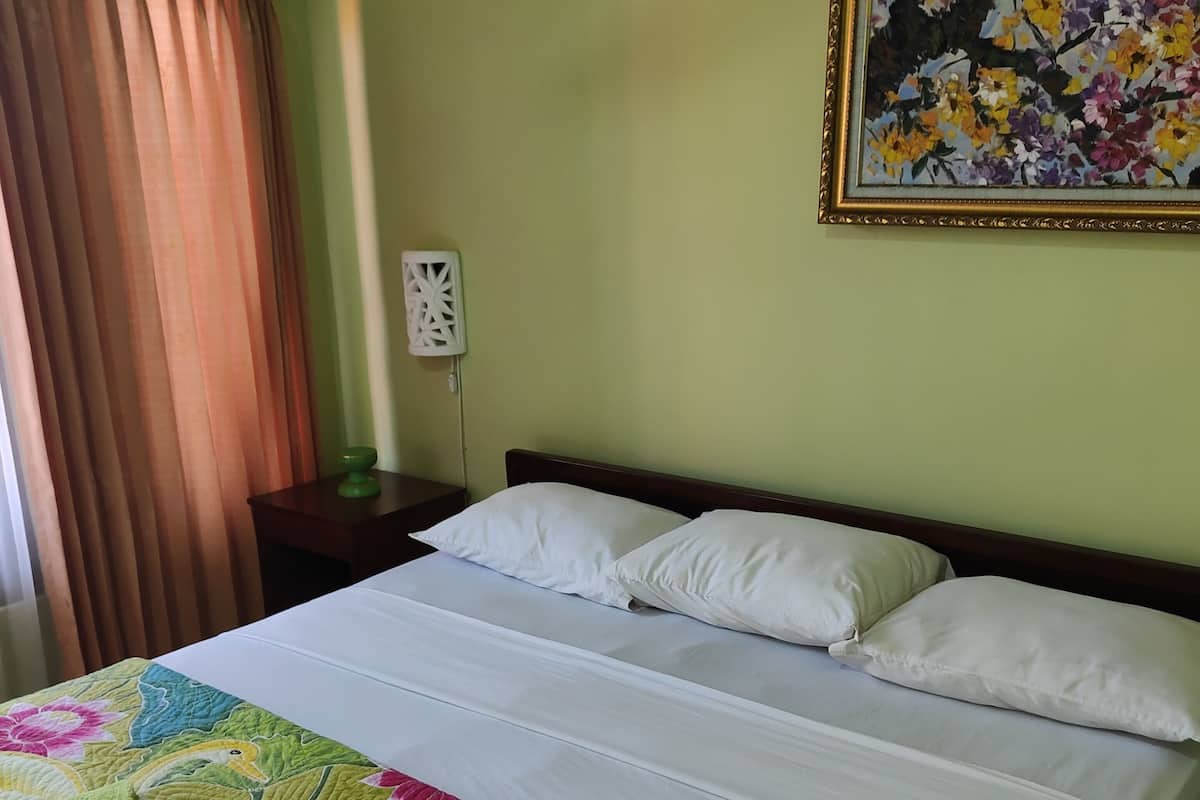A neatly made bed with a floral bedspread, a green towel, and a nightstand with a lamp.