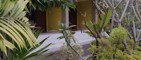 A courtyard with a yellow building, surrounded by various plants and trees.