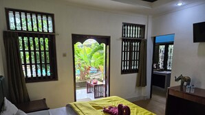 Une chambre d’hôtel avec un lit, un bureau et une vue sur un jardin, visible à travers la porte.