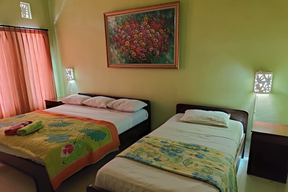 Two single beds with floral bedspreads, a painting of flowers on the wall, and a window with curtains.