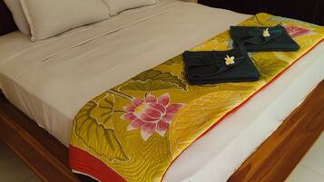 A bed with a floral bedspread, white pillows, and neatly folded towels on a wooden bed frame.