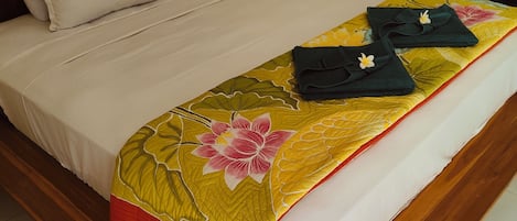 A bed with a floral bedspread, white pillows, and neatly folded towels on a wooden bed frame.