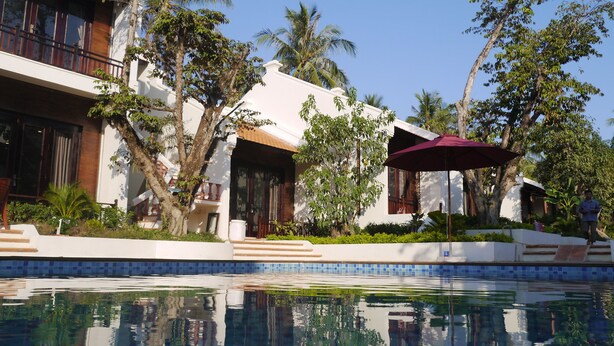 A resort with a swimming pool, palm trees, and a white building with balconies.