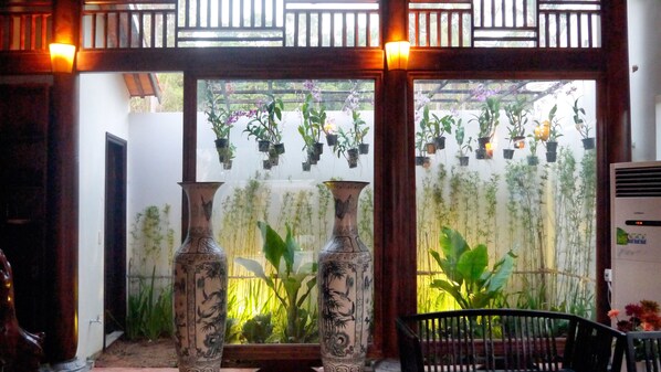 A room with two large vases, a wooden partition with hanging plants, and a view of greenery outside.