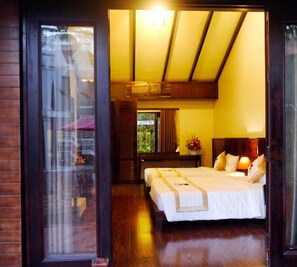A hotel room with a large bed, a wooden floor, a window, and a view of the outdoors.