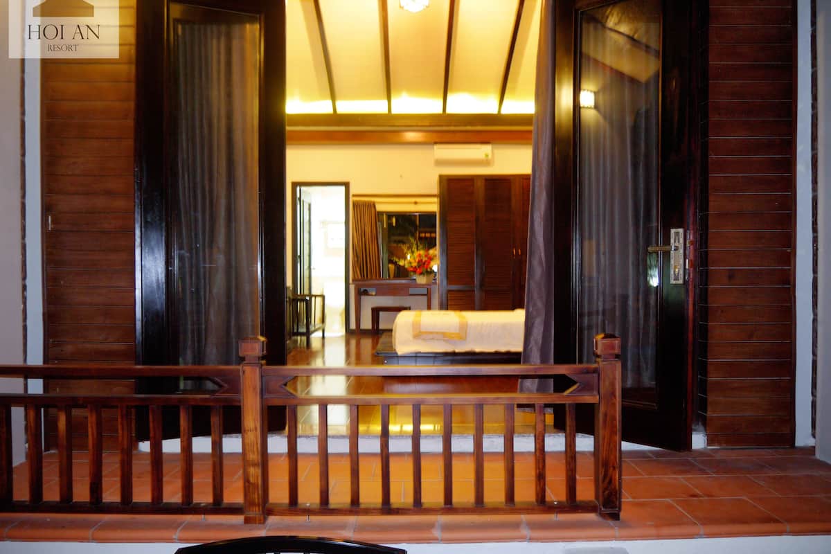 A hotel room with a wooden floor, a bed, a desk, and a view of the outside.