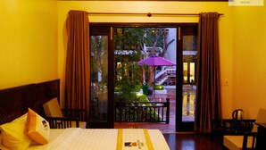 A hotel room with a bed, a desk, a chair, and a view of the outside balcony.