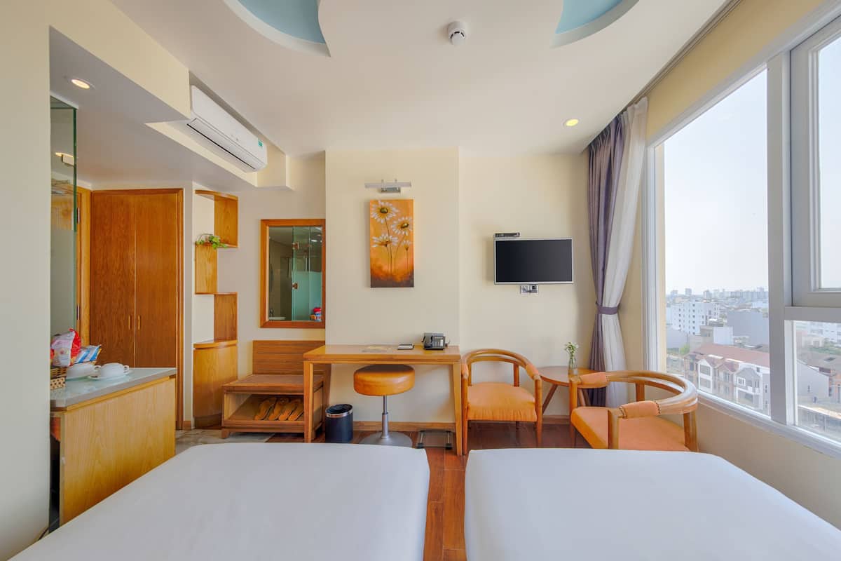 A hotel room with two beds, a desk, a chair, a TV, and a large window with a city view.