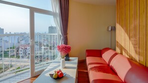 A modern room with a red sofa, a table with a vase of flowers, and a view of the city through large windows. - Sea Queen Hotel (Da Nang)