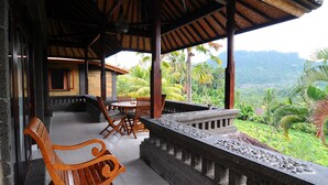 A covered outdoor seating area with wooden furniture and a stone balustrade overlooking a lush landscape. - Villa Lihat Sawah (Sidemen)