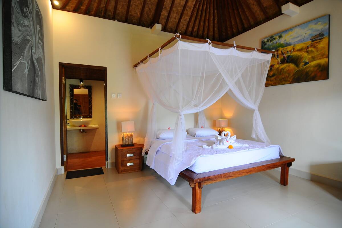 A bedroom with a four-poster bed, a wooden bench, bedside tables, and a painting on the wall.