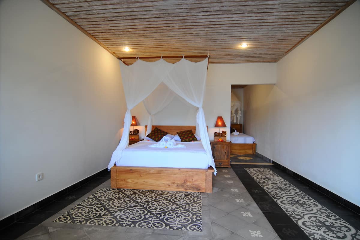 A bedroom with a wooden bed frame, a canopy bed, patterned floor tiles, and bedside lamps.