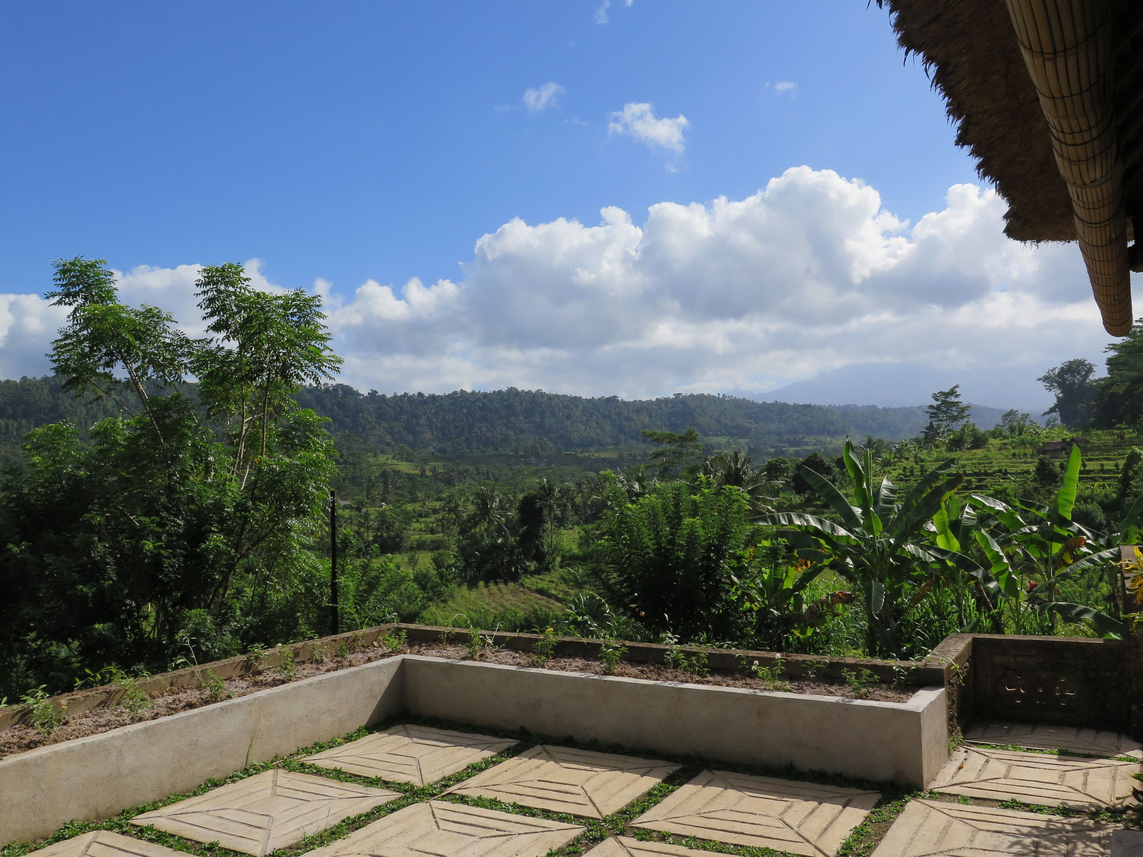A terrace with a view of a lush landscape, including trees and a distant mountain range.