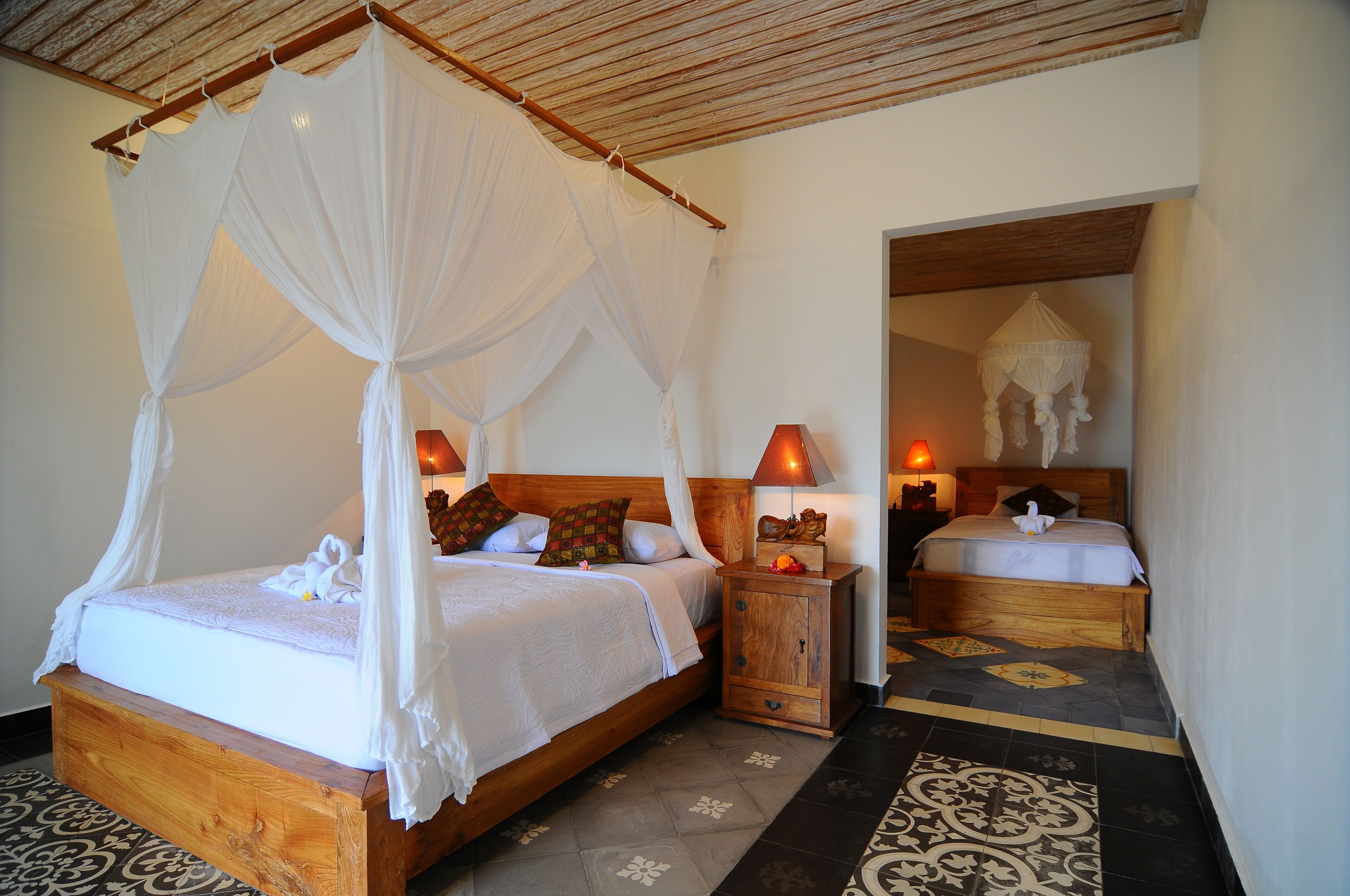 A bedroom with a four-poster bed, a nightstand with a lamp, and a mirror.