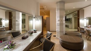 Un amplio vestíbulo de hotel con un mostrador de recepción de mármol, varias zonas de estar y grandes espejos que reflejan el espacio.