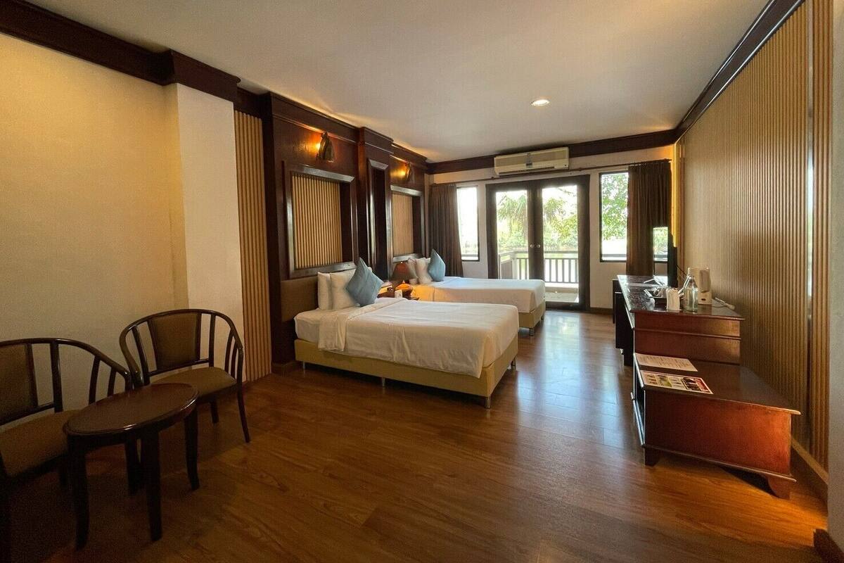 A hotel room with two beds, a desk, chairs, and a balcony with a view.