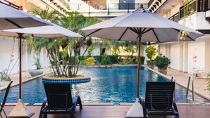 Zona de piscina con dos sillones de playa y sombrillas, rodeada de plantas y una piscina.