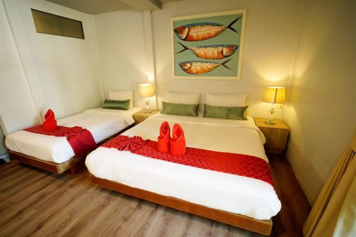 A hotel room with two beds, each with a red towel and pillow. There are nightstands with lamps, and a painting of fish on the wall.