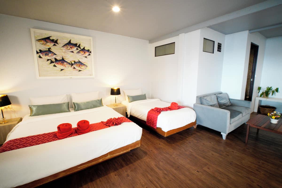 Une chambre d’hôtel avec deux lits, un canapé gris, une table basse en bois et un tableau au mur.