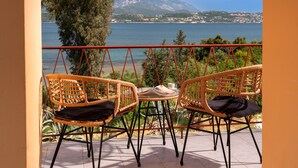 Un balcon agrémenté de fauteuils en osier et d’une petite table, offrant une vue sur une étendue d’eau et un paysage montagneux.