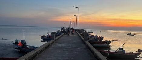 A pier extending into calm waters at sunset with boats docked on both sides.