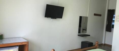A room with a bed, a small desk with a computer, a television mounted on the wall, and a mirror above the desk.