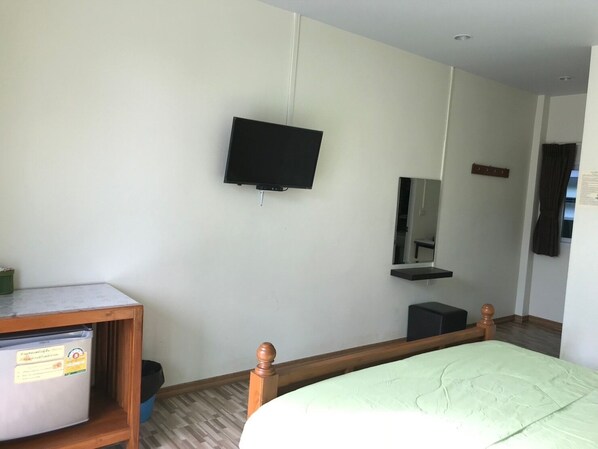 A room with a bed, a small desk with a computer, a television mounted on the wall, and a mirror above the desk.