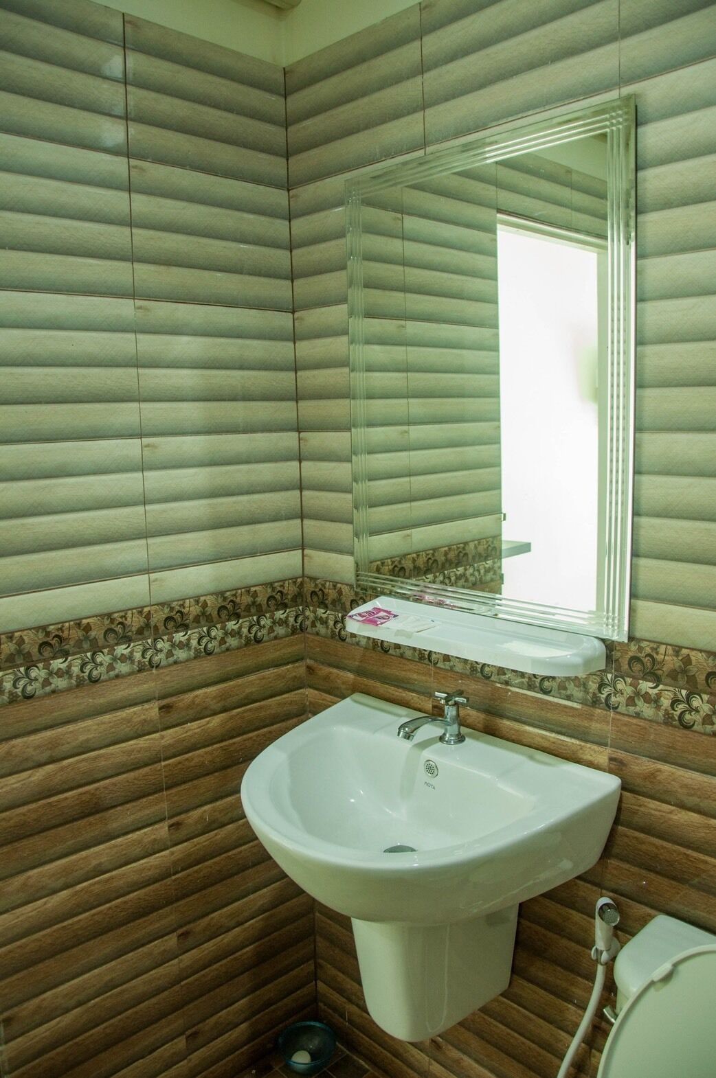 Un baño con pared de paneles de madera, un lavabo blanco con un espejo encima y un inodoro a la derecha.