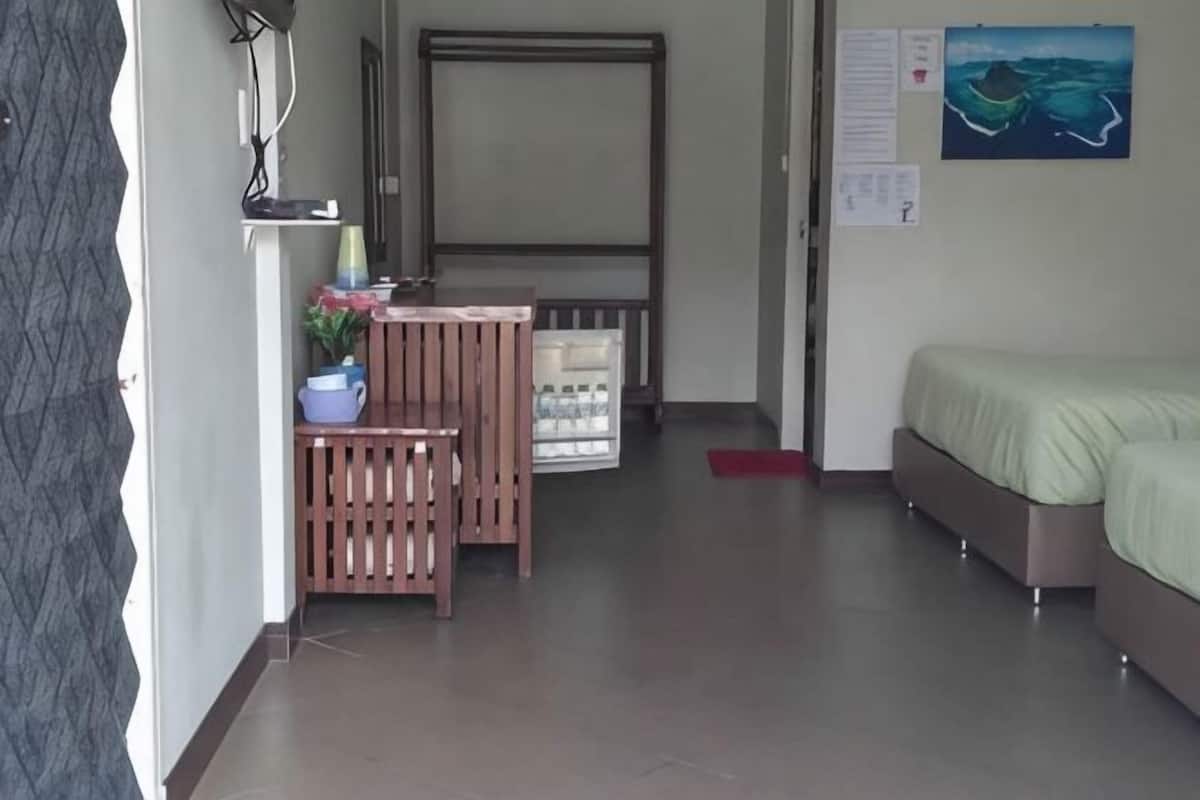 Una habitación con cama, escritorio, silla, una mesita con planta y una puerta.