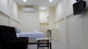 A small, compact room with a bed, a chair, a table, and a TV mounted on the wall. - The Cube Resort (Chanthaburi)