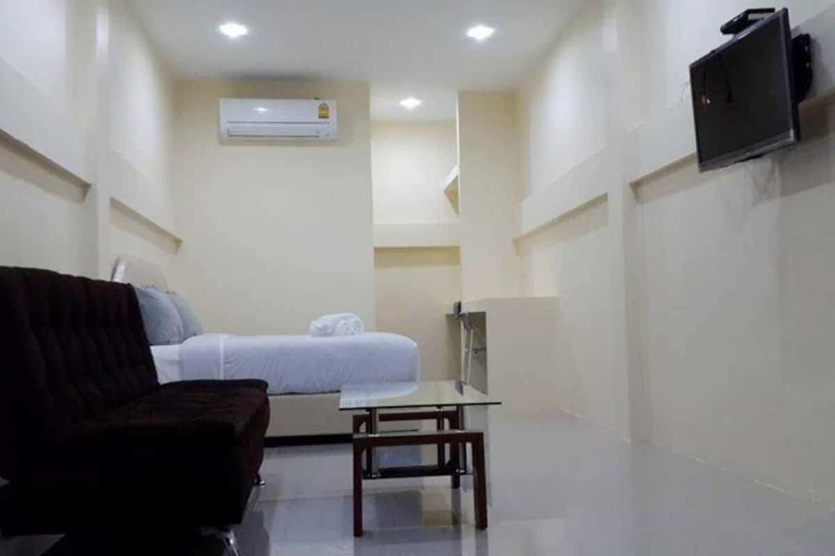 A small, compact room with a bed, a chair, a table, and a TV mounted on the wall.
