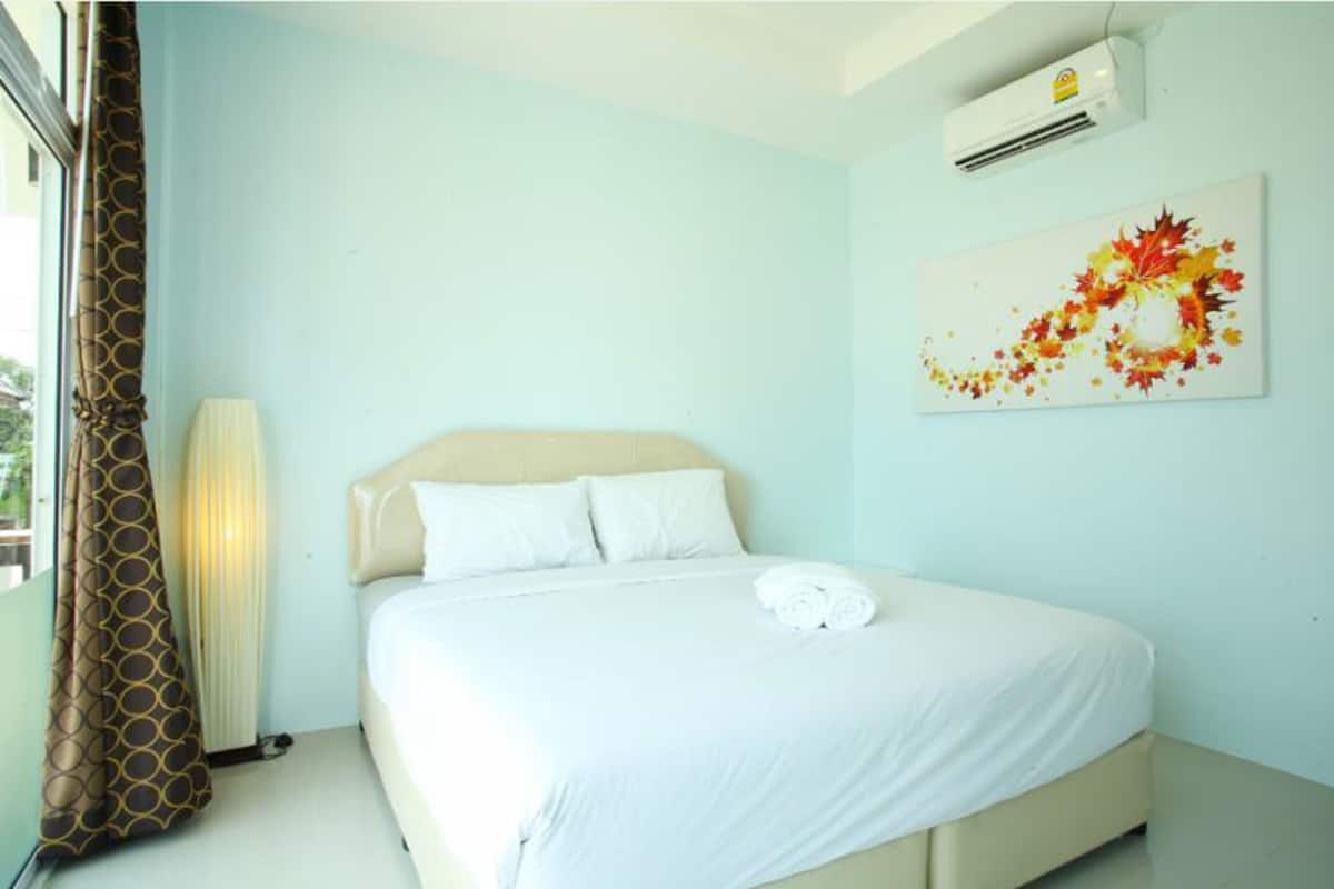 A hotel room with a bed, a window with curtains, an air conditioner, and a wall-mounted artwork.