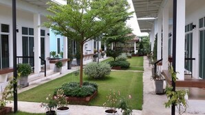 A covered outdoor area with a central pathway, surrounded by potted plants and a small lawn. - The Cube Resort (Chanthaburi)