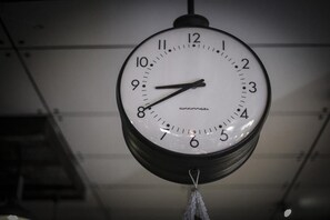 A wall-mounted clock with a white face and black numbers, hanging from a ceiling with a visible metal structure. - Tamajun Hotel (Chanthaburi)