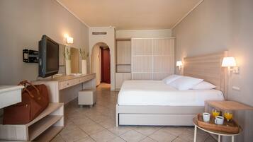 A hotel room with a bed, bedside table with a tray of breakfast, a desk with a TV, a wardrobe, and a bathroom visible through an archway.