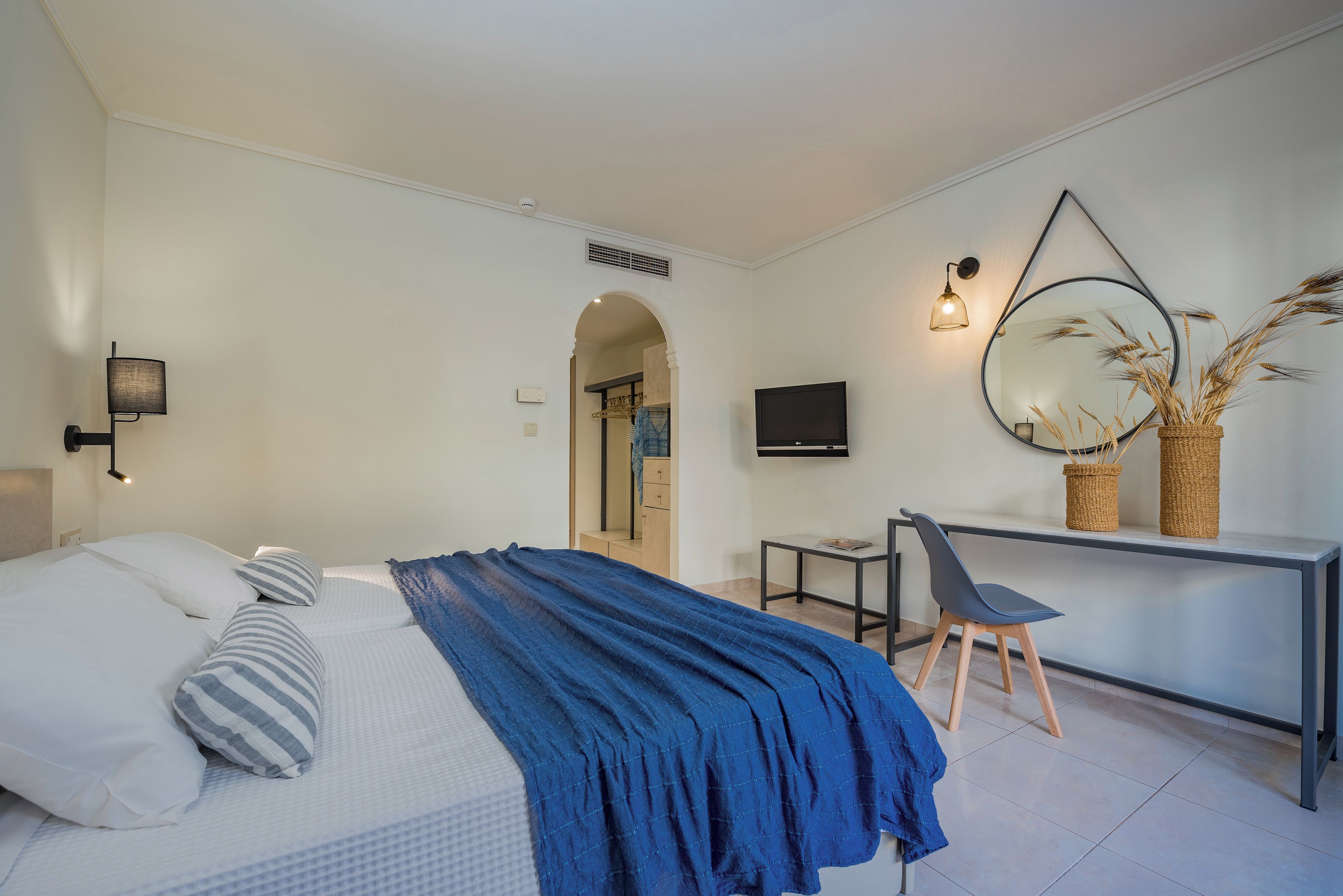 A modern bedroom with a bed, desk, chair, and a large mirror.