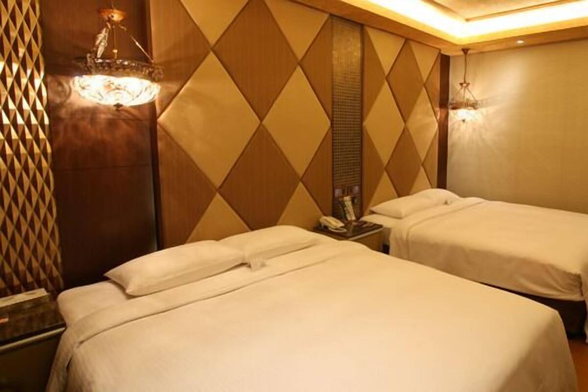 A hotel room with two beds, a patterned wall, and a small table with a phone and a lamp.