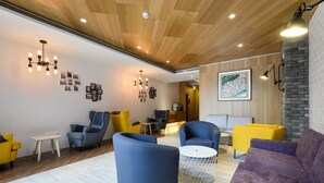 Un área de estar moderna con sillones azules y amarillos, un sofá morado y una mesa redonda.