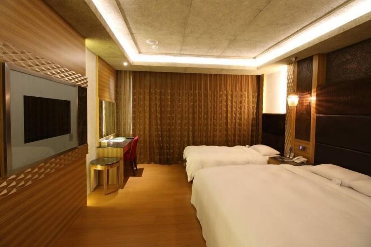 A hotel room with two beds, a desk with a chair, a mirror, and a television.
