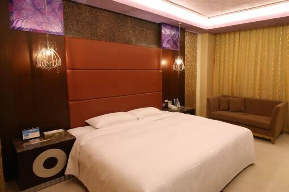 A hotel room with a large bed, a sofa, two wall-mounted lamps, and a curtain.