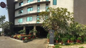 Un hotel de varios pisos con diseño moderno, que cuenta con una entrada ajardinada con diversas plantas y una vista despejada de la fachada del edificio.