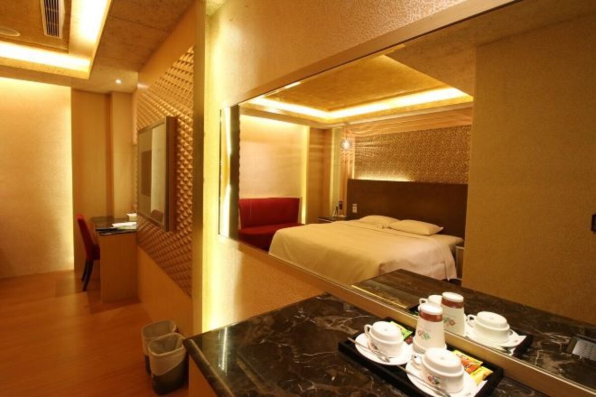 A hotel room with a bed, a desk, and a dining area with a tray of breakfast items.