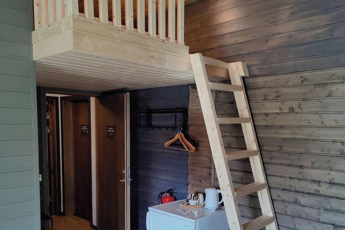 A compact room with a lofted sleeping area, a small kitchenette, and a wooden ladder.