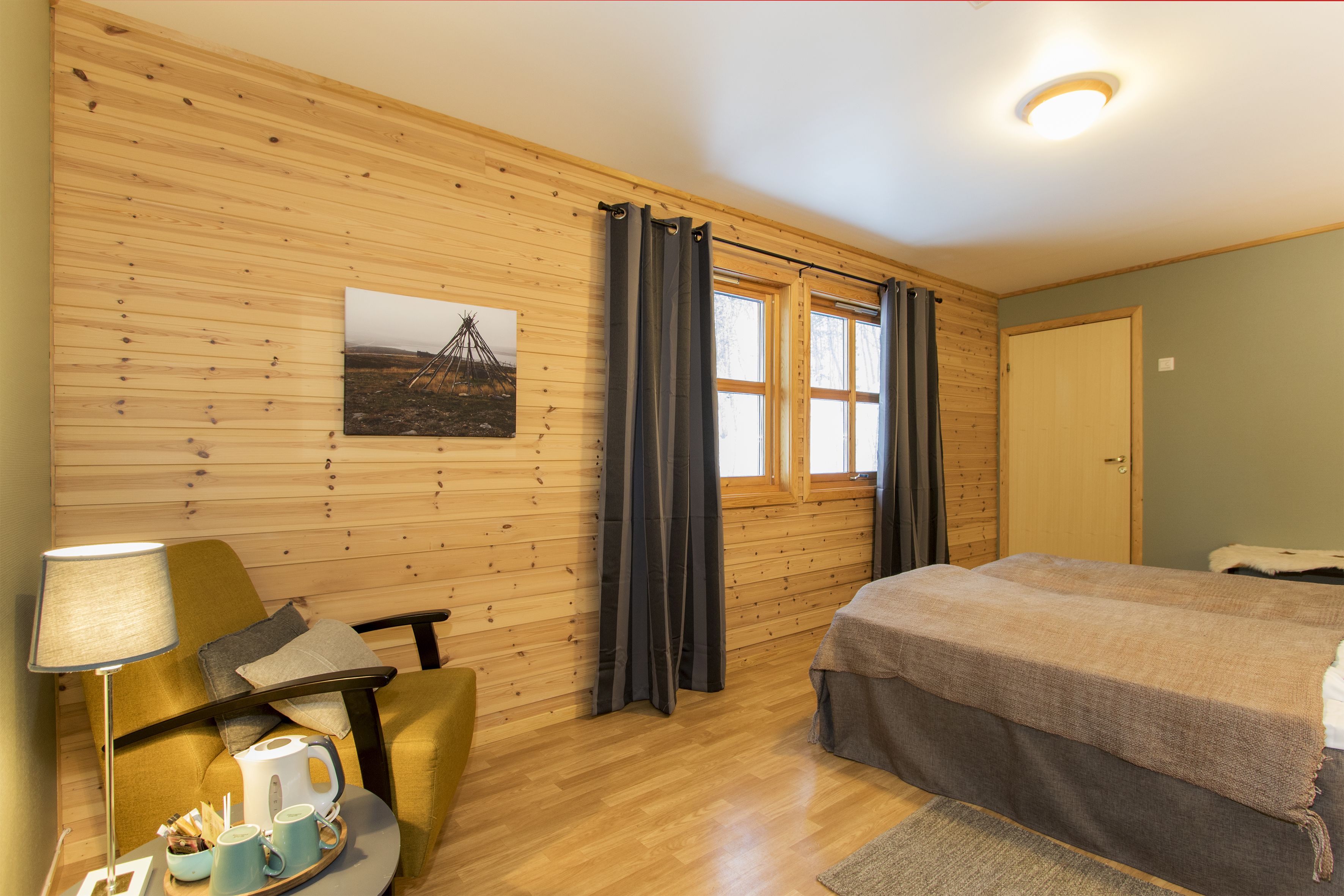 Ein gemütliches Zimmer mit Holzwänden, einem Bett, einem Schreibtisch mit Lampe und einem Fenster mit Vorhängen.