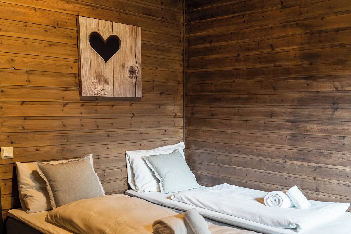 A room with two beds, wooden walls, and a heart-shaped decoration.