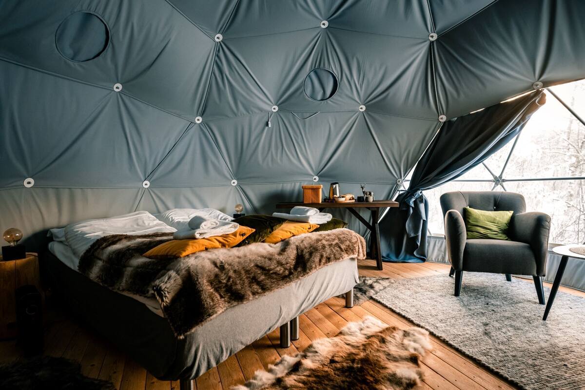 A cozy tent-style room with a bed, a chair, and a small table with a lamp.